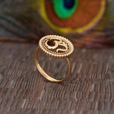 a gold ring with an om sign on it sitting in front of a peacock feather