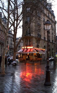 an empty street with people walking around and buildings in the background at dusk, on a rainy day