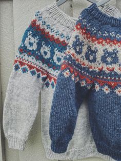 two knitted sweaters are hanging on a clothesline, one is blue and the other is white