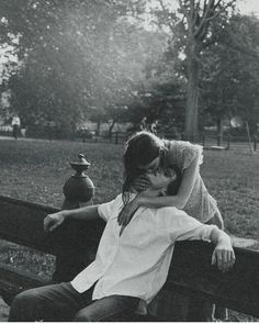 black and white photograph of two people sitting on a bench in a park, one kissing the other