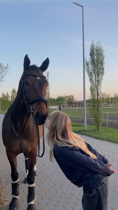 a woman standing next to a brown horse on top of a brick walkway in front of a green field