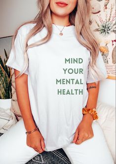 Introducing our Mind Your Mental Health t-shirt, the perfect way to spread awareness and support mental well-being in style. Crafted from soft, breathable fabric, this comfortable tee is a great reminder to prioritize your mental health. Whether you're lounging at home or out running errands, this shirt will keep you feeling positive and empowered. Wear it proudly and start conversations about the importance of self-care and mental wellness. Available in a variety of sizes, this t-shirt makes a Meaningful Graphic Print Short Sleeve T-shirt, Meaningful Short Sleeve Graphic T-shirt, Casual Graphic T-shirt For Awareness Events, Casual Graphic Print T-shirt For Awareness Events, Casual T-shirt With Graphic Print For Awareness Events, Meaningful Short Sleeve T-shirt With Letter Print, Empowering Text Print Crew Neck T-shirt, Empowering Short Sleeve T-shirt With Text Print, White Cotton T-shirt For Awareness Events