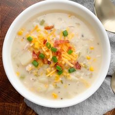 a white bowl filled with soup and cheese on top of a wooden table next to spoons