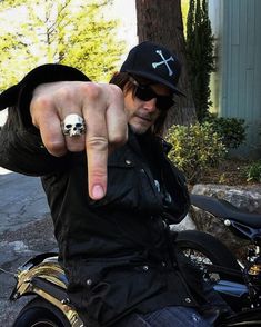 a man pointing at the camera while sitting on a motorbike with a skull ring in his hand