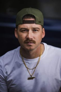 a man with a mustache wearing a white t - shirt and a green baseball cap