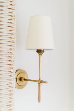 a wall light with a white lamp shade on it's side and a wicker basket behind it