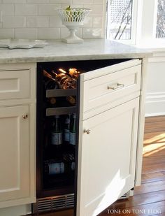 an open cabinet in the middle of a kitchen with white cabinets and wood flooring