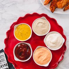 four different sauces in small bowls on a red platter next to chicken wings