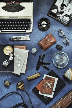 an old fashioned typewriter surrounded by other items on a blue tablecloth with writing utensils