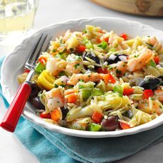 a white bowl filled with pasta salad next to a glass of water and a red handled utensil