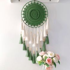 a green and white wall hanging with tassels next to a vase filled with flowers