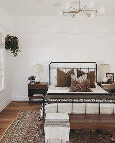 a bedroom with white walls and wood flooring has a black metal bed frame, two nightstands, and a rug on the floor