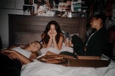 two young women sitting on a bed with pizza and drinks in front of them,