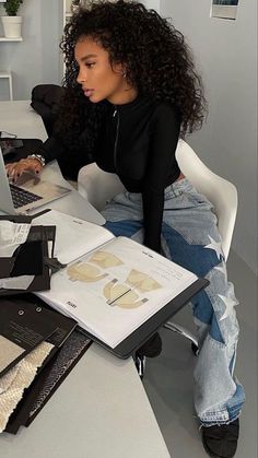 a woman sitting at a table with a laptop and papers in front of her,