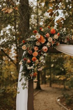 a wedding arch decorated with flowers and greenery for an outdoor ceremony in the woods