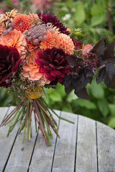 a bouquet of flowers sitting on top of a wooden table in front of some bushes