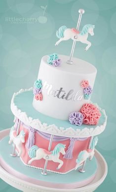 a three tiered cake decorated with pink, blue and white icing has a horse on top