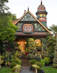 a green house with lots of plants and bushes around it's front door, surrounded by greenery