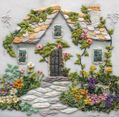 a house made out of flowers and plants on a white cloth with embroidered trimmings