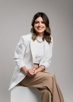 a woman sitting on top of a white stool wearing a skirt and blazer jacket