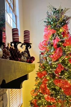 a decorated christmas tree in front of a window with red and green ribbons on it