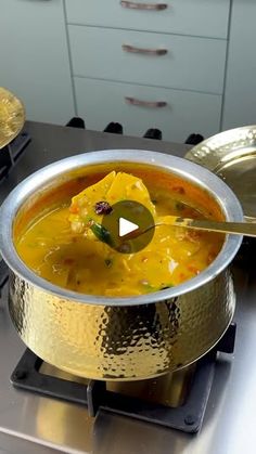 a metal bowl filled with soup on top of a stovetop next to gold dishes