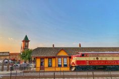 a red and white train traveling past a yellow building with a clock tower in the background