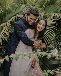 a man and woman embracing in front of palm trees