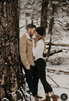 a man and woman standing next to a tree in the snow