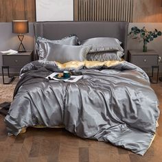 a bed with silver sheets and pillows on top of it in a room that has wooden floors