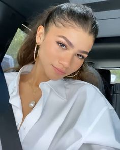 a woman sitting in the back seat of a car wearing gold hoop earrings and a white shirt