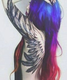 a woman with colorful hair and tattoos on her back is posing in front of a white wall