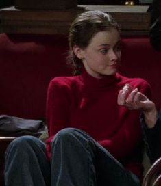 a woman sitting on a red couch eating food from a white plate in front of her