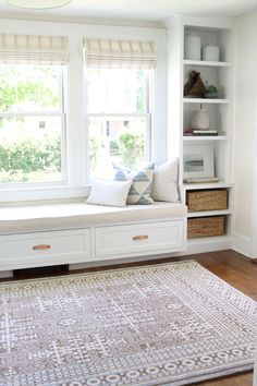 a window seat with pillows on it in front of a white bookcase filled with books