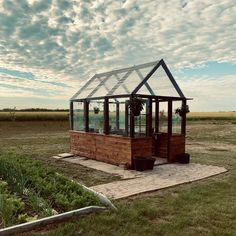 a small wooden structure with a glass roof in the middle of an open field on a cloudy day