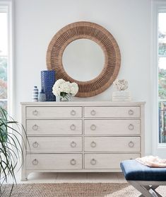 a white dresser with blue and white vases on top of it next to a round mirror