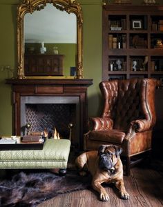 a dog is sitting on the floor in front of a chair and fireplace with a mirror above it