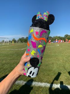 someone is holding up a mickey mouse can cooler at a soccer field with other people in the background