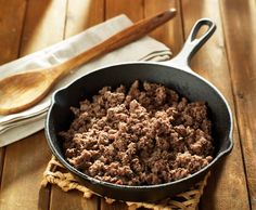 a pan filled with meat sitting on top of a wooden table next to a spatula