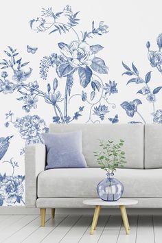 a white couch sitting in front of a blue and white wallpaper with flowers on it