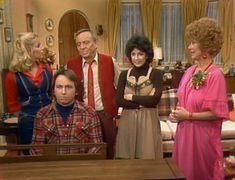 four people standing in front of a table with an adult looking at the camera and one person wearing a pink dress