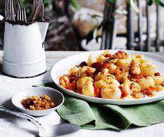 a white plate topped with pasta and sauce next to a cup filled with seasoning