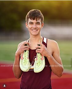 a young man holding two pairs of shoes in his hands and smiling at the camera