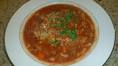 a white plate topped with pasta and meat soup covered in parmesan cheese on top of a granite counter