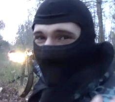 a man wearing a black hat and scarf in the woods with his face covered by a mask