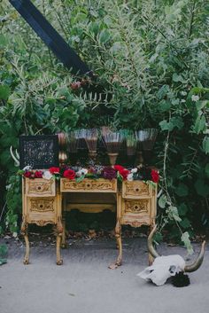 an old desk with flowers on it is surrounded by greenery