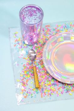 a table set with confetti and a glass on the placemat, next to a silver spoon