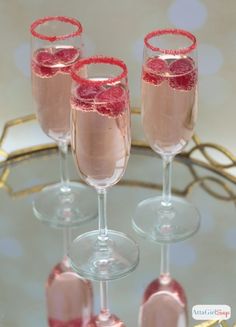 three wine glasses filled with pink liquid and garnished with red glitters on the rim