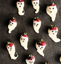 strawberries are arranged in the shape of ghost heads on a black surface with white icing