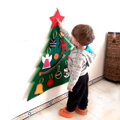 a little boy standing in front of a christmas tree made out of paper and cardboard